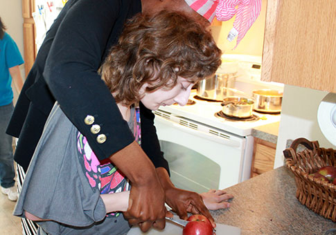 A person supported by CSS cuts an apple with assistance from a direct support professional.